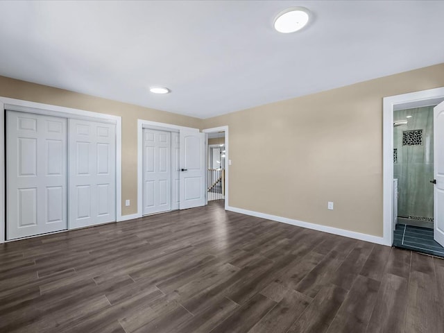 unfurnished bedroom with multiple closets, dark wood-type flooring, and ensuite bath