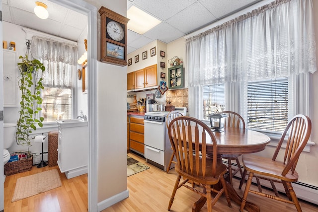 dining space with baseboard heating, a paneled ceiling, a healthy amount of sunlight, and light hardwood / wood-style floors