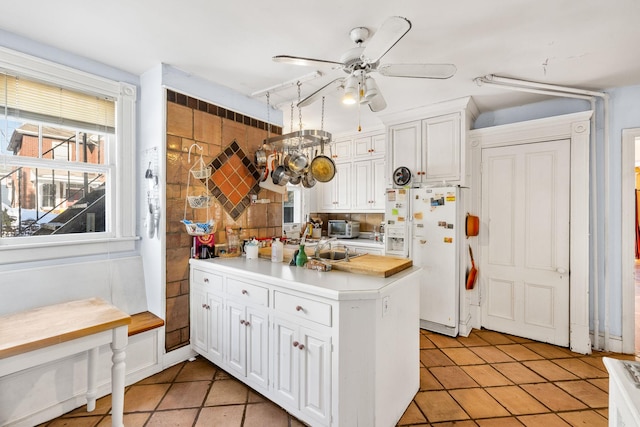 kitchen with sink, ceiling fan, white cabinetry, white fridge with ice dispenser, and kitchen peninsula