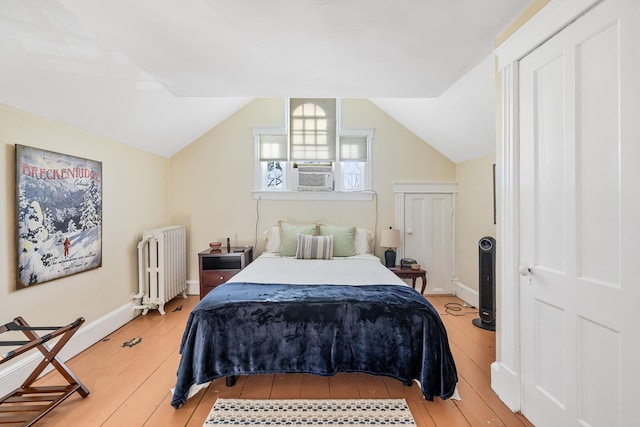 bedroom featuring vaulted ceiling, radiator heating unit, light hardwood / wood-style floors, and cooling unit