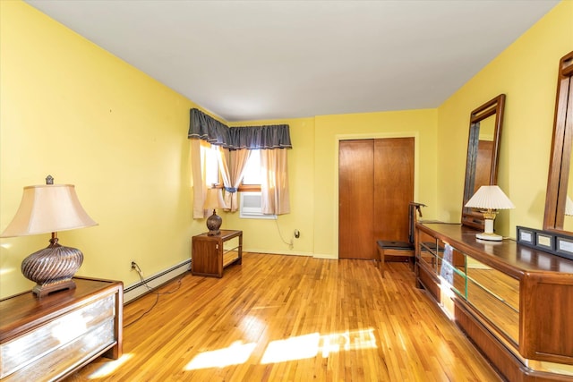 bedroom featuring a baseboard radiator, light hardwood / wood-style flooring, cooling unit, and a closet