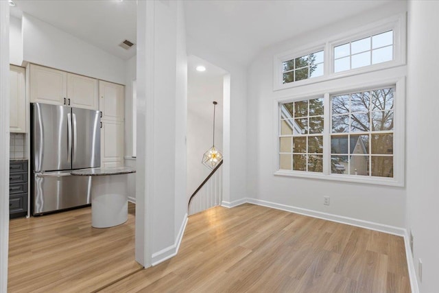 interior space featuring pendant lighting, stainless steel refrigerator, lofted ceiling, backsplash, and light hardwood / wood-style floors