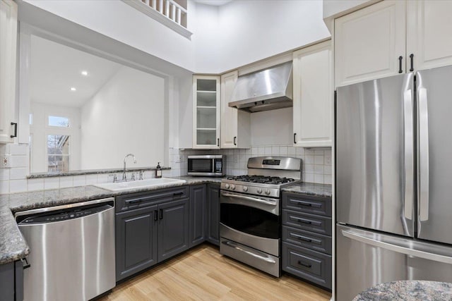 kitchen with wall chimney exhaust hood, stainless steel appliances, gray cabinets, and dark stone counters