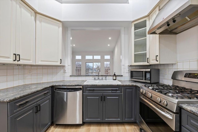 kitchen featuring sink, extractor fan, dark stone countertops, appliances with stainless steel finishes, and gray cabinets