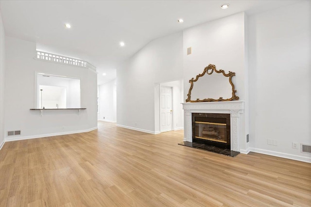 unfurnished living room with high vaulted ceiling, a high end fireplace, and light hardwood / wood-style floors