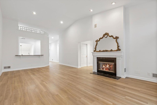 unfurnished living room with light hardwood / wood-style flooring, a high end fireplace, and high vaulted ceiling