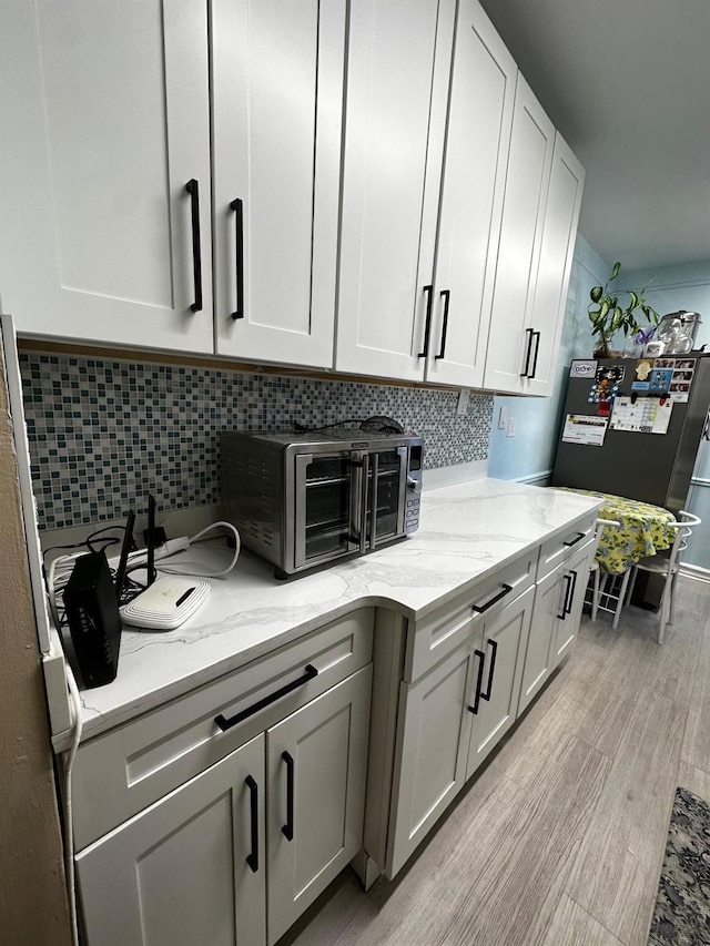 kitchen featuring tasteful backsplash, refrigerator, light stone counters, and light hardwood / wood-style flooring