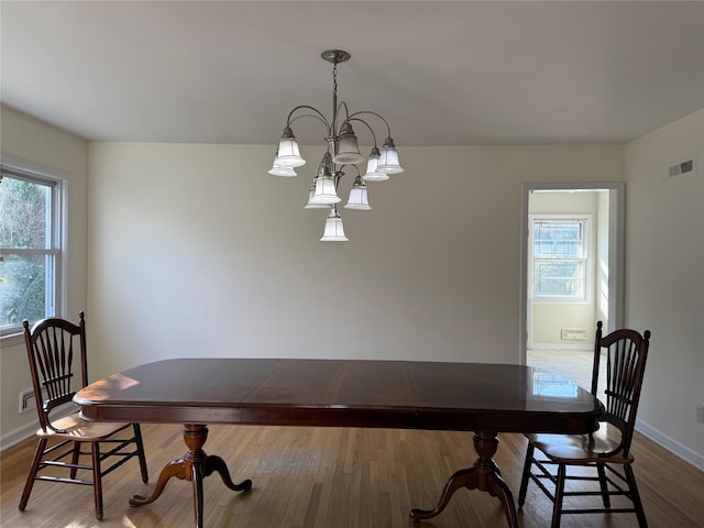 dining space with a healthy amount of sunlight, a notable chandelier, and hardwood / wood-style floors