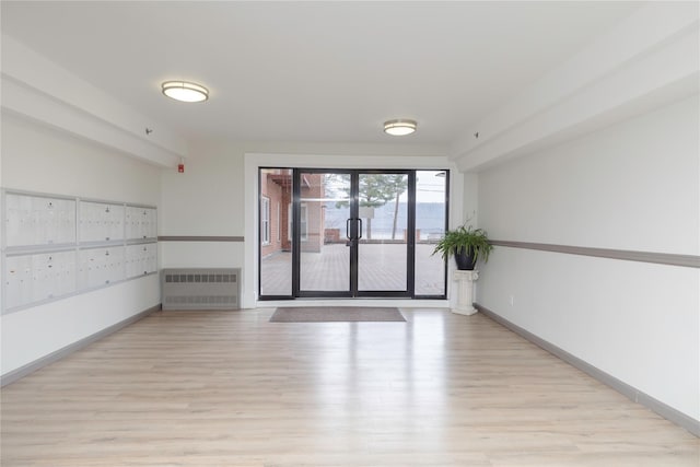 unfurnished room featuring a mail area, radiator heating unit, and light hardwood / wood-style floors