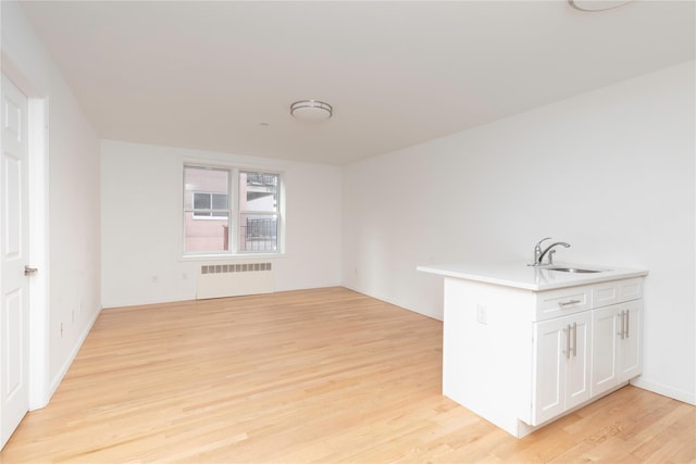 interior space with white cabinetry, radiator, sink, and light hardwood / wood-style flooring