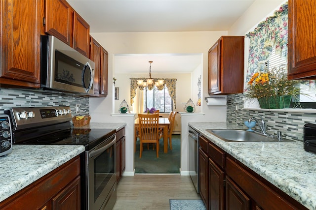 kitchen featuring pendant lighting, appliances with stainless steel finishes, an inviting chandelier, sink, and backsplash