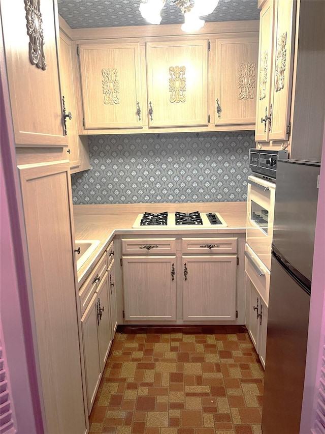 kitchen featuring wall oven, light brown cabinets, backsplash, stainless steel refrigerator, and white gas stovetop