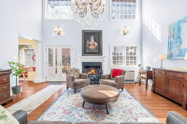 living room featuring a high end fireplace, french doors, a high ceiling, light wood finished floors, and ornate columns