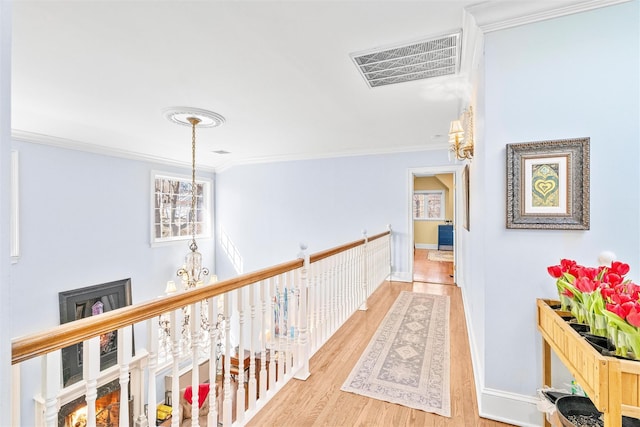 corridor featuring visible vents, a notable chandelier, ornamental molding, wood finished floors, and baseboards