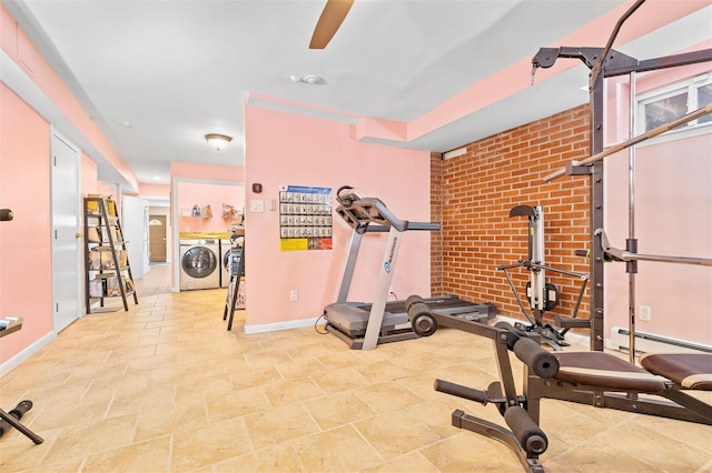 exercise area with a baseboard heating unit, baseboards, brick wall, and washing machine and clothes dryer