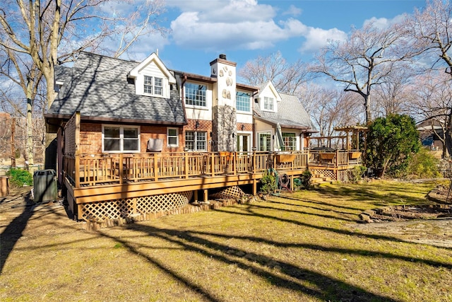 rear view of property with brick siding, roof with shingles, a chimney, a deck, and a yard