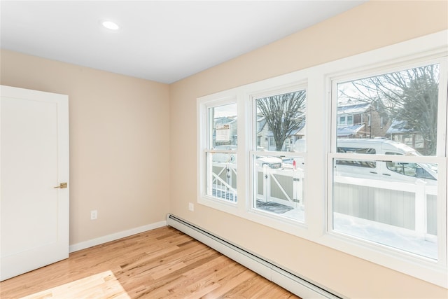 spare room featuring baseboard heating and light hardwood / wood-style flooring