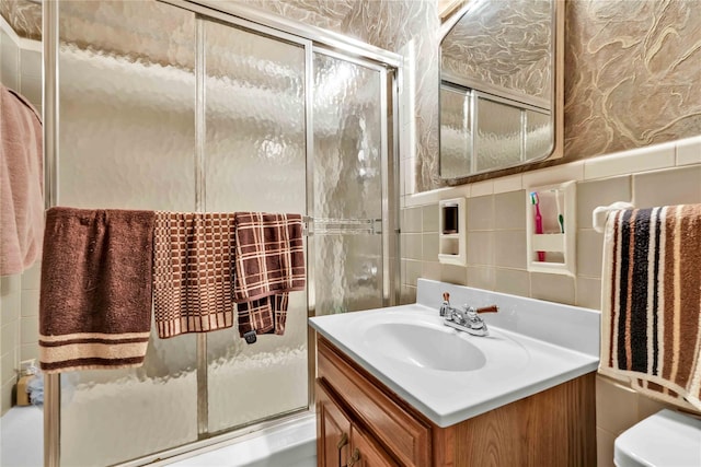 full bathroom with toilet, combined bath / shower with glass door, tile walls, and vanity