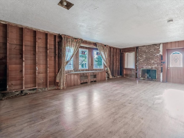 unfurnished living room with radiator, a textured ceiling, a fireplace, and wood walls