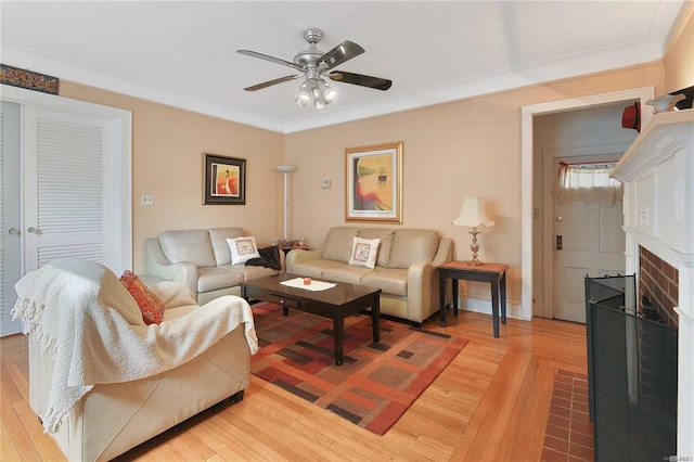 living room featuring ceiling fan, light wood-type flooring, a brick fireplace, and ornamental molding