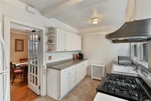 kitchen featuring black range with gas stovetop, white cabinets, beam ceiling, and sink