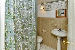 bathroom with curtained shower, tile patterned floors, toilet, and tile walls