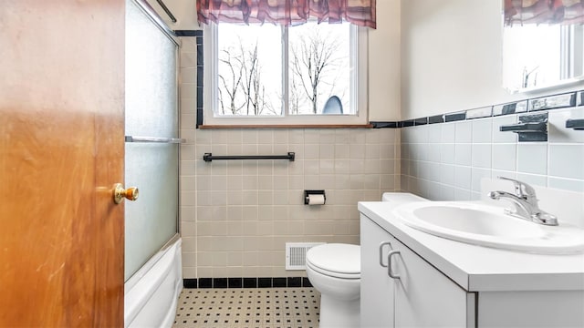 full bathroom with toilet, a healthy amount of sunlight, tile walls, and vanity