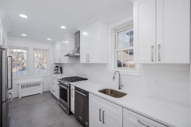 kitchen featuring sink, white cabinetry, radiator heating unit, stainless steel appliances, and wall chimney exhaust hood