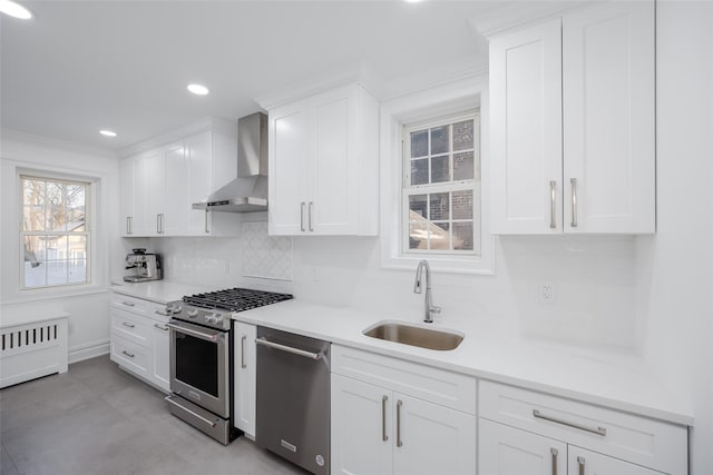 kitchen featuring sink, wall chimney range hood, white cabinets, stainless steel appliances, and backsplash