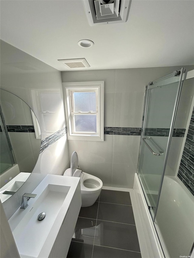 full bathroom featuring tile patterned floors, vanity, tile walls, toilet, and combined bath / shower with glass door