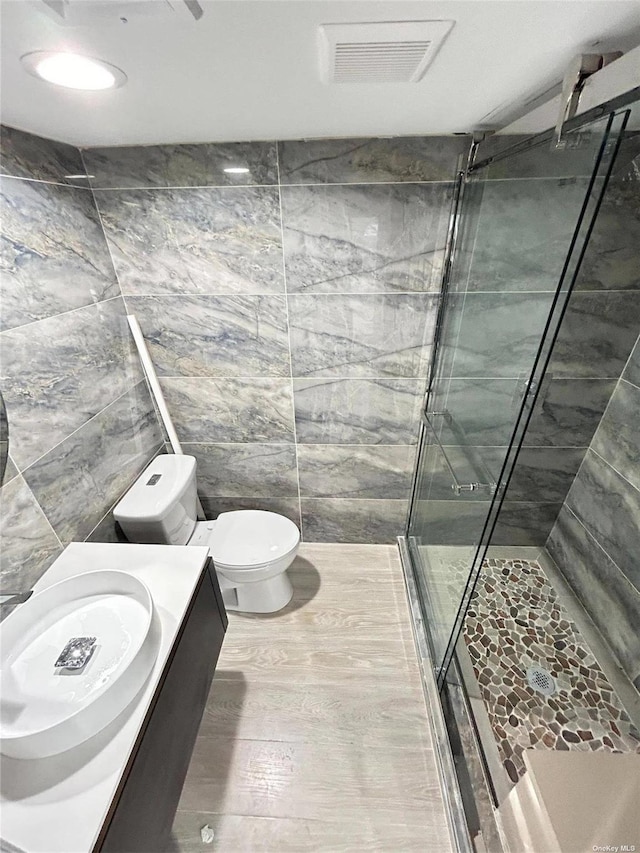 bathroom featuring a shower with door, tile walls, toilet, and vanity