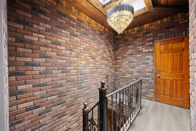 hallway featuring brick wall, a chandelier, and light hardwood / wood-style flooring