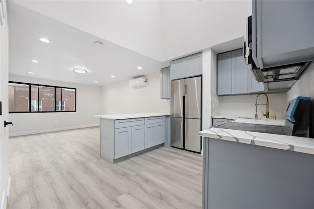 kitchen with kitchen peninsula, gray cabinetry, stainless steel refrigerator, an AC wall unit, and sink