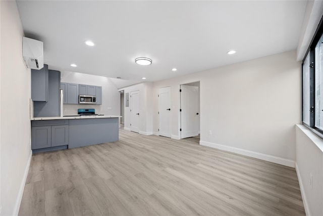 kitchen featuring light hardwood / wood-style floors, kitchen peninsula, stainless steel appliances, gray cabinetry, and an AC wall unit