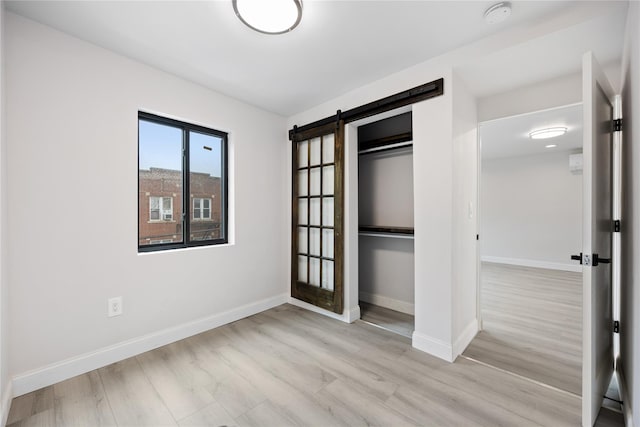 unfurnished bedroom featuring light wood-type flooring, a barn door, and a closet