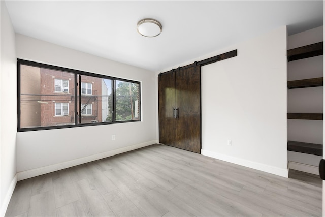 unfurnished bedroom with a barn door and light wood-type flooring