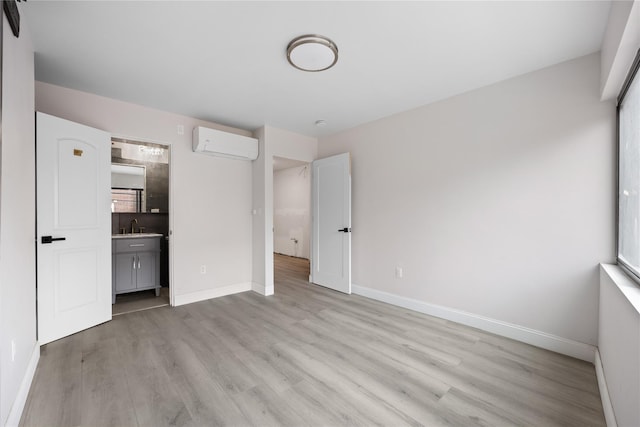 unfurnished bedroom with an AC wall unit, connected bathroom, and light hardwood / wood-style flooring