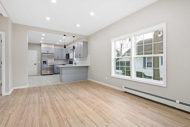 kitchen featuring a baseboard heating unit, sink, hanging light fixtures, stainless steel fridge, and light hardwood / wood-style flooring