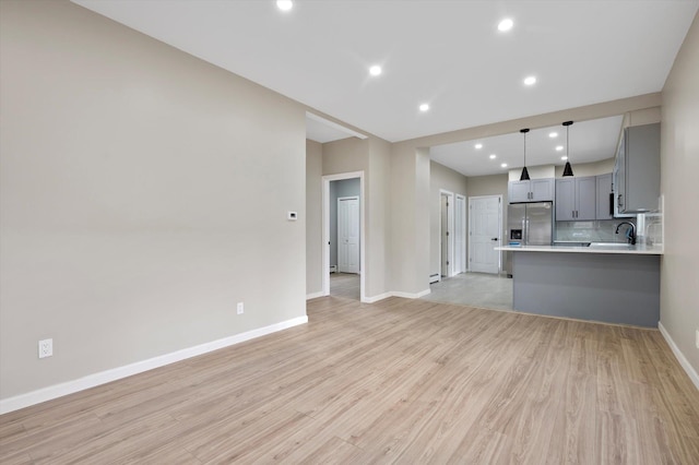 unfurnished living room with baseboard heating, light hardwood / wood-style flooring, and sink