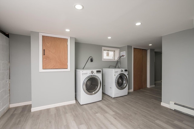 clothes washing area with a baseboard radiator, separate washer and dryer, and light hardwood / wood-style flooring