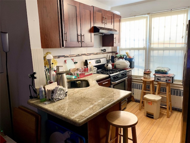 kitchen featuring light hardwood / wood-style floors, stainless steel gas range, backsplash, a kitchen breakfast bar, and light stone countertops