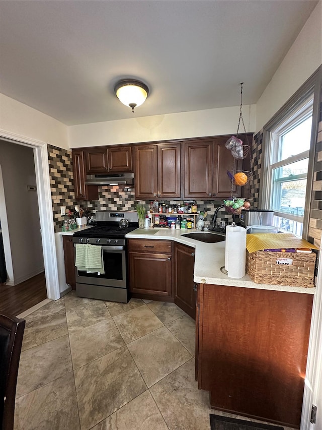 kitchen featuring stainless steel gas range oven, decorative backsplash, decorative light fixtures, dark brown cabinetry, and sink