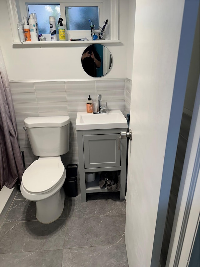 bathroom featuring toilet, vanity, and tile walls