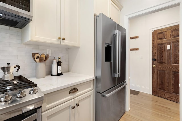 kitchen with light stone counters, decorative backsplash, stainless steel appliances, and light hardwood / wood-style floors