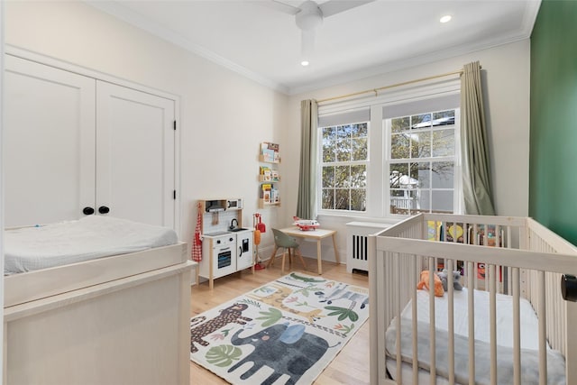 bedroom with ornamental molding, a closet, ceiling fan, light hardwood / wood-style floors, and a crib