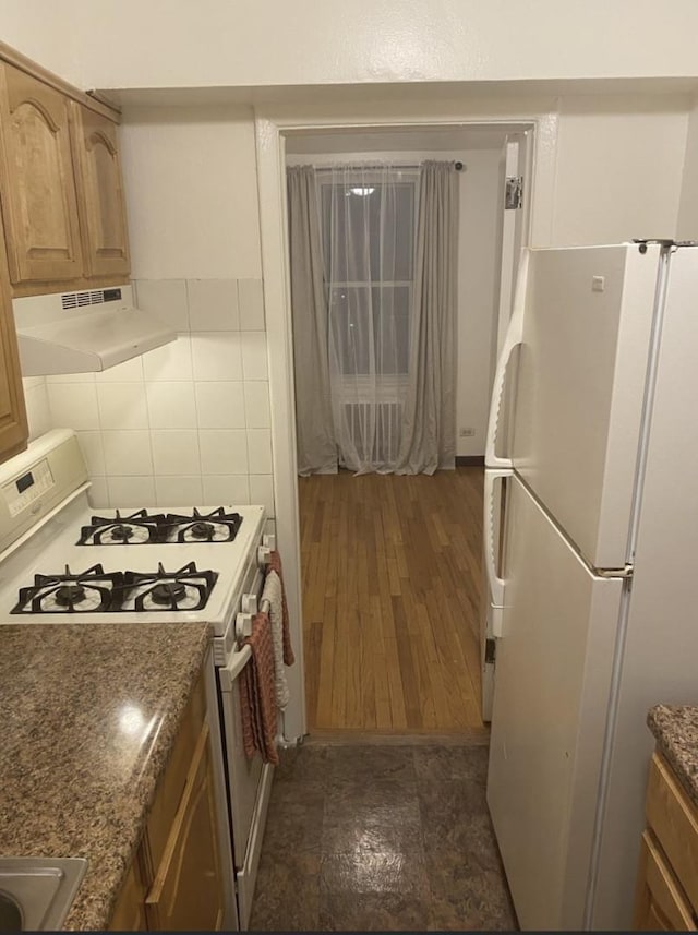 kitchen with backsplash, dark wood-type flooring, dark stone countertops, and white appliances