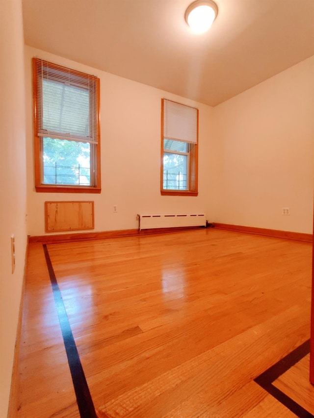 unfurnished room with a baseboard heating unit and hardwood / wood-style floors