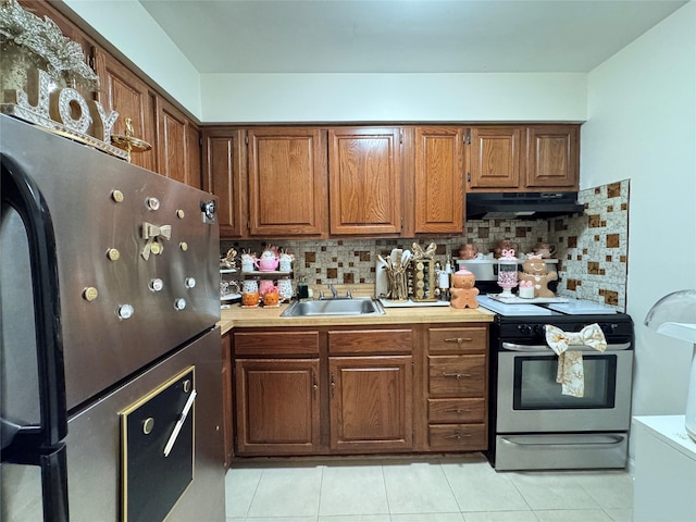 kitchen with backsplash, fridge, sink, light tile patterned flooring, and stainless steel range