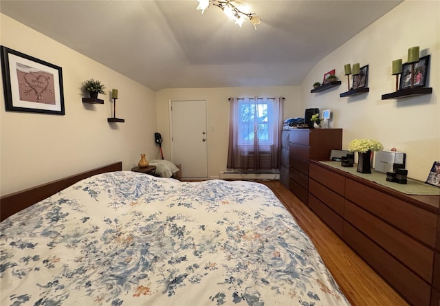 bedroom with wood-type flooring, lofted ceiling, and a baseboard heating unit