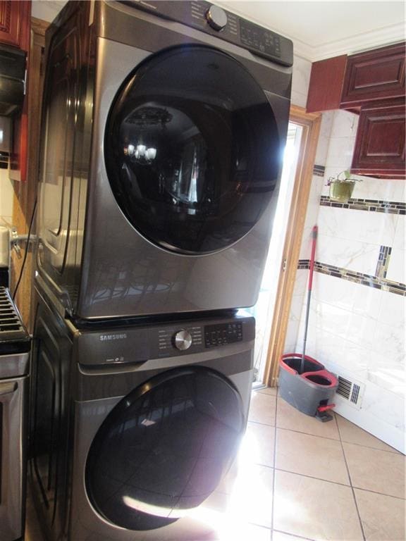 washroom featuring light tile patterned floors, stacked washer / drying machine, and ornamental molding